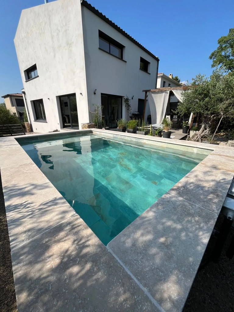 Piscine 10m² avec banquette de repos et carrelage Bali. margelles en travertin